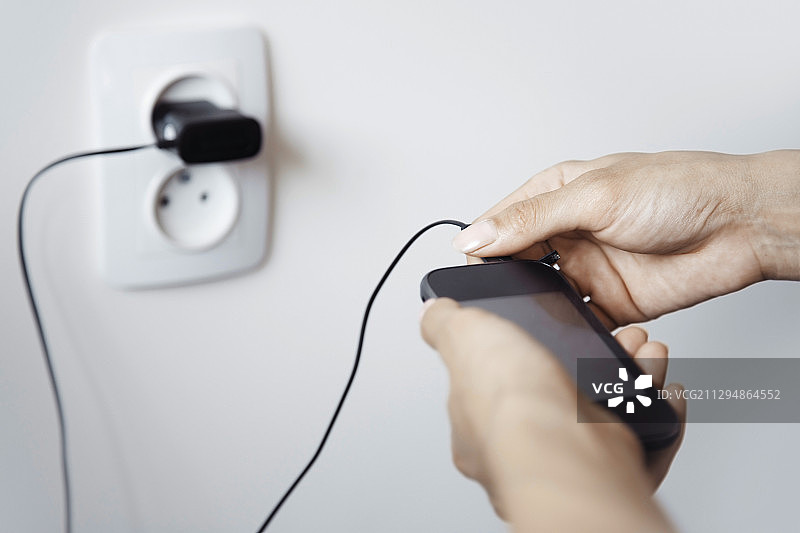 人手拿着连接电源线的智能手机图片素材