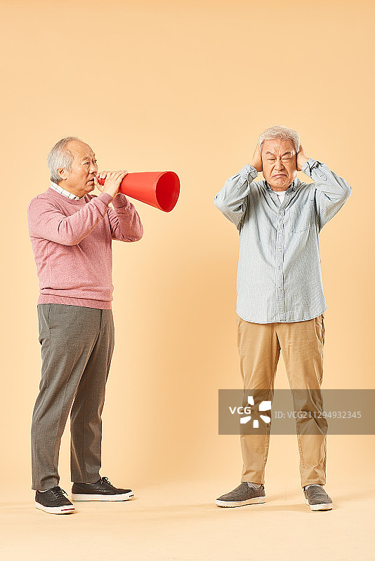 两位年长的男人站在一起，一个用扩音器对着另一个大喊，另一个人捂住耳朵图片素材