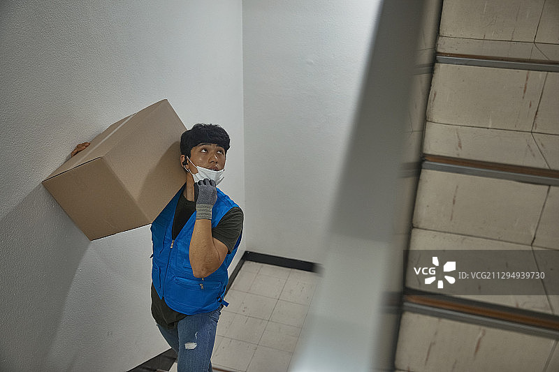 男人送货员在楼梯上爬楼梯，戴着口罩，因新冠感到呼吸困难图片素材