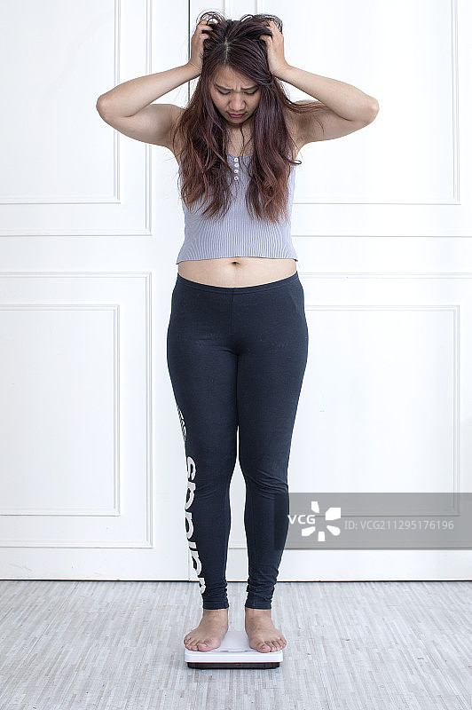 东方女性手放头上站在体重机上量体重图片素材