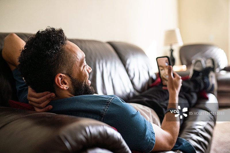 黑人男子在家中沙发上使用手机图片素材