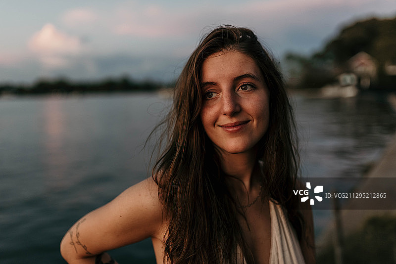 日落时分，在美国科菲维尔的湖边，对着天空微笑的年轻女子肖像图片素材