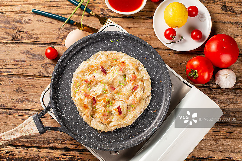 一片美味手抓饼放在木板背景上的平底锅里图片素材