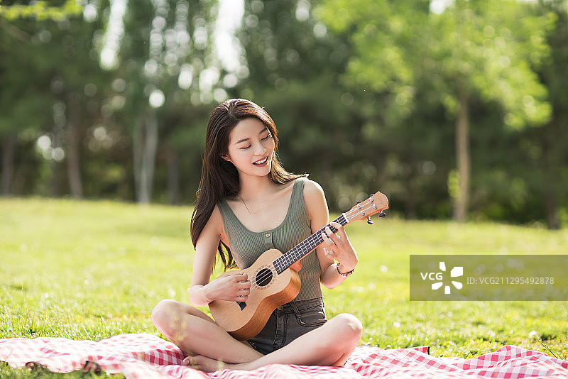 美丽的年轻女子坐在草地上弹奏尤克里里图片素材