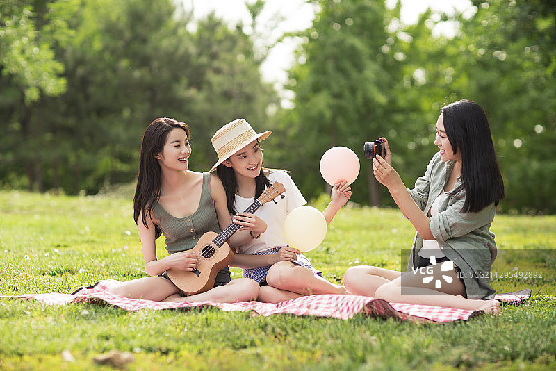 闺蜜在草地上使用数码相机拍照图片素材