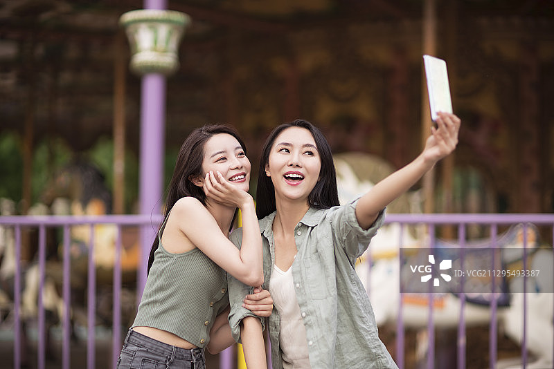 闺蜜在游乐场使用智能手机自拍图片素材