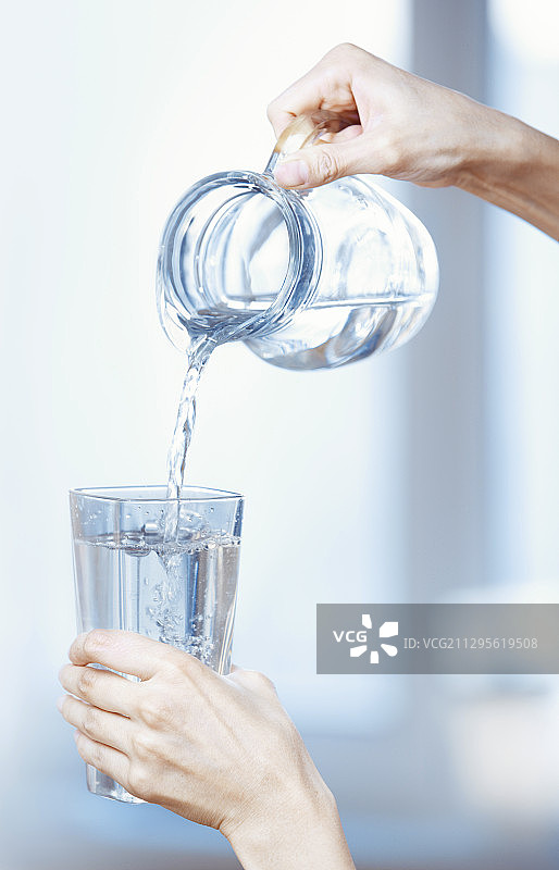 人手将水从罐子倒入玻璃杯中图片素材
