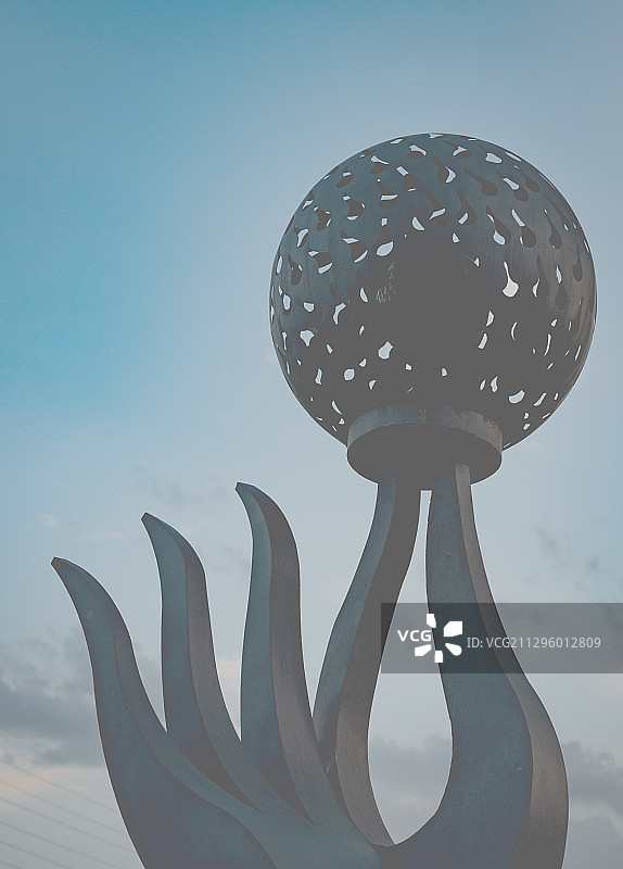 对着蓝色的天空，雕塑手的食指与拇指捏着圆形的灯笼。图片素材