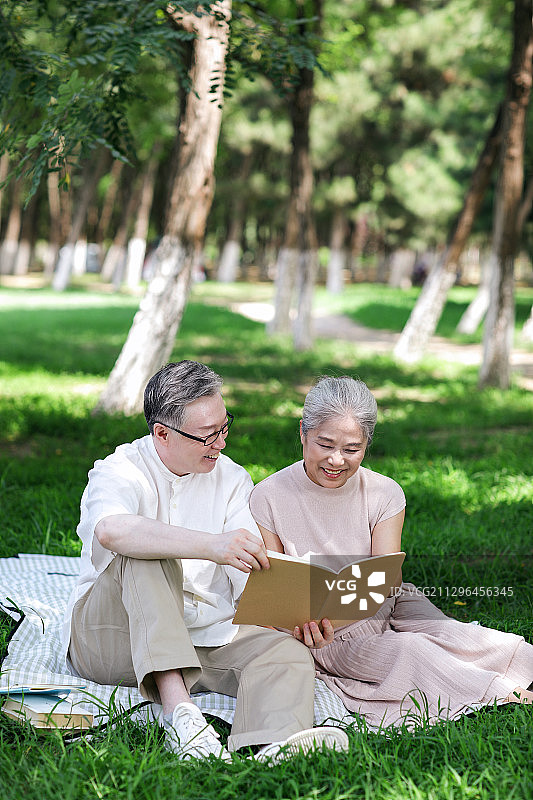 幸福的老年夫妇坐在公园草地上看书图片素材