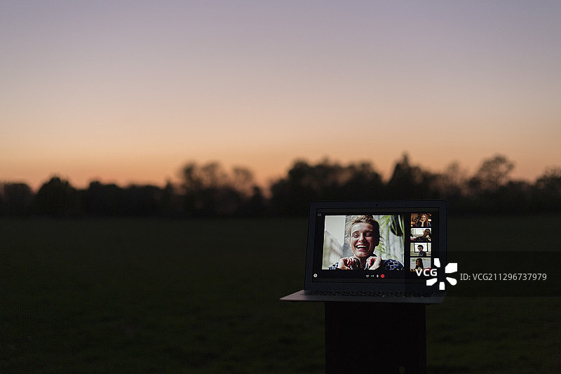 朋友们在黄昏时分在公园里用笔记本电脑屏幕进行视频聊天图片素材