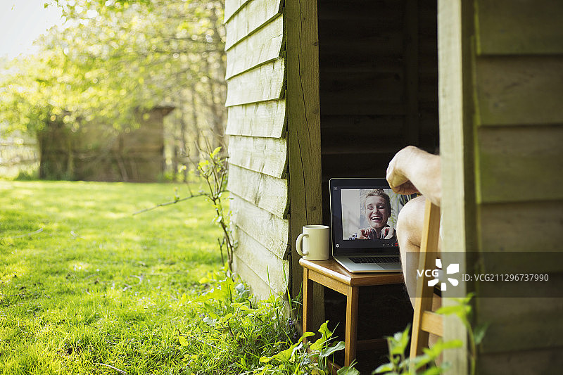 男子在花园棚屋里用笔记本电脑与朋友视频聊天图片素材