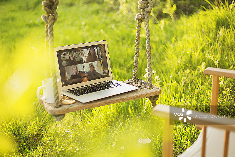 同事在花园的秋千上通过笔记本电脑屏幕进行视频聊天图片素材