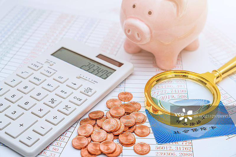 阳光下的小猪存钱罐、硬币、计算器、放大镜和医保卡图片素材