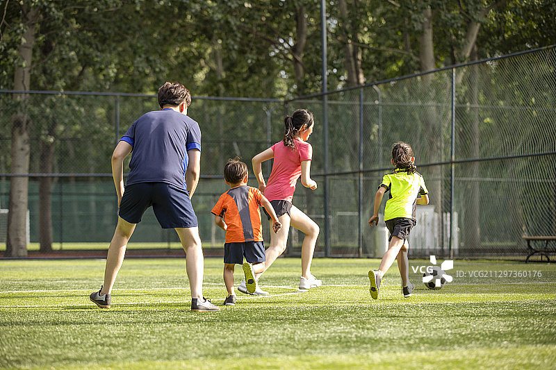 快乐的年轻家庭在足球场踢足球图片素材