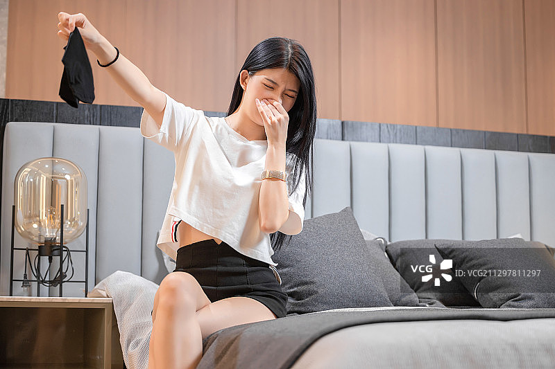 坐在床上，感觉衣服有异味的亚洲女孩图片素材