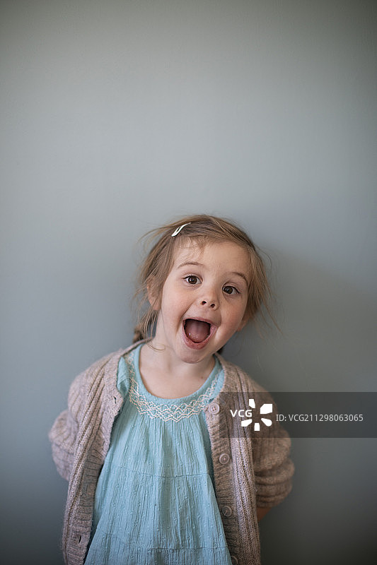 对着蓝色墙壁做鬼脸的小女孩肖像图片素材