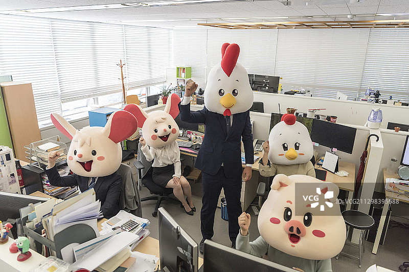 办公室里戴着猪、老鼠、鸡面具的商人和女商人做出欢呼的手势图片素材