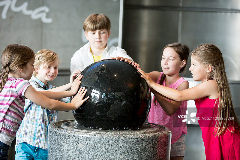 孩子们在科学考察旅行中触摸博物馆里地球仪上的水图片素材