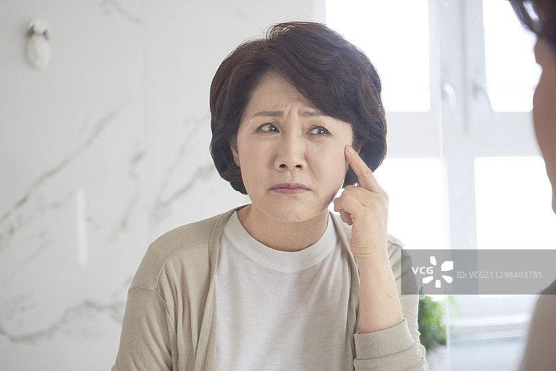 中年妇女照镜子检查脸上的皱纹图片素材