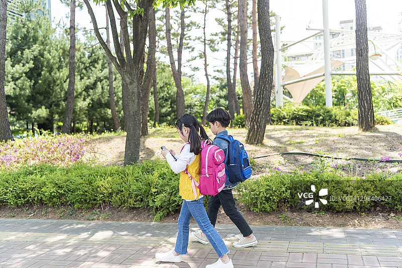 男孩和女孩走在街上，看着智能手机图片素材