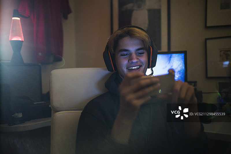 微笑的青少年戴着耳机在卧室里使用智能手机图片素材