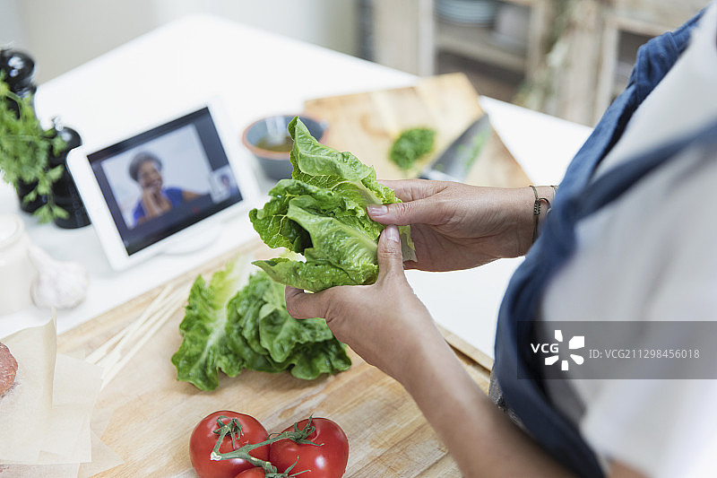 在厨房用平板电脑烹饪和视频聊天的女人图片素材