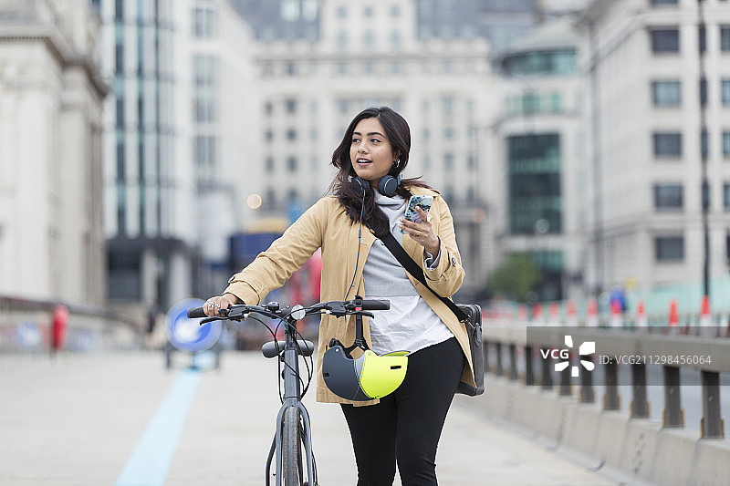 女人在城市桥梁上推自行车用智能手机图片素材