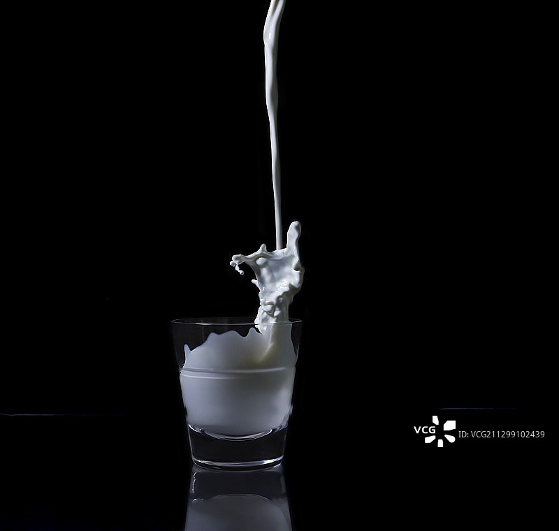 黑色背景下玻璃杯中倾倒的牛奶特写，美国布雷登顿图片素材