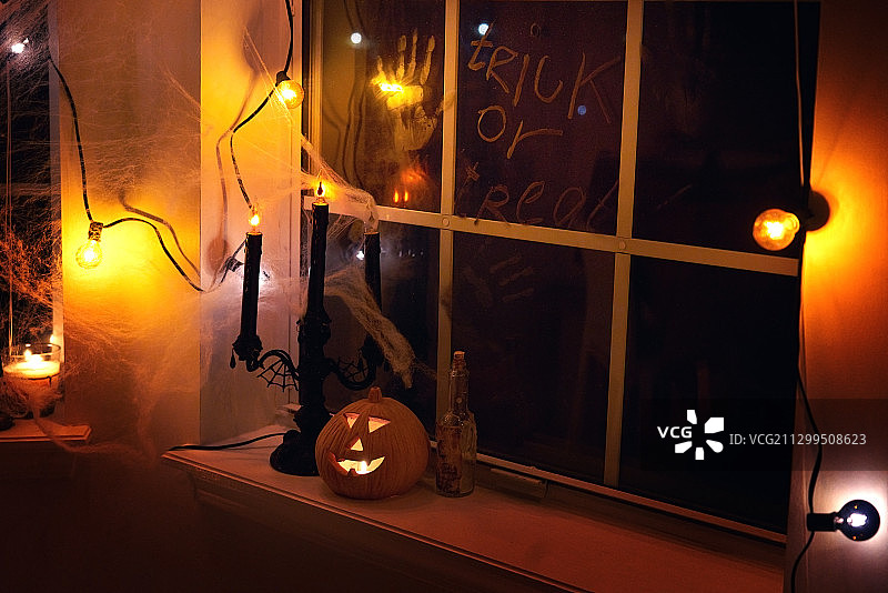 万圣节灯光照亮窗台上的南瓜灯和烛台，窗户上有手印和不给糖就捣蛋字样图片素材