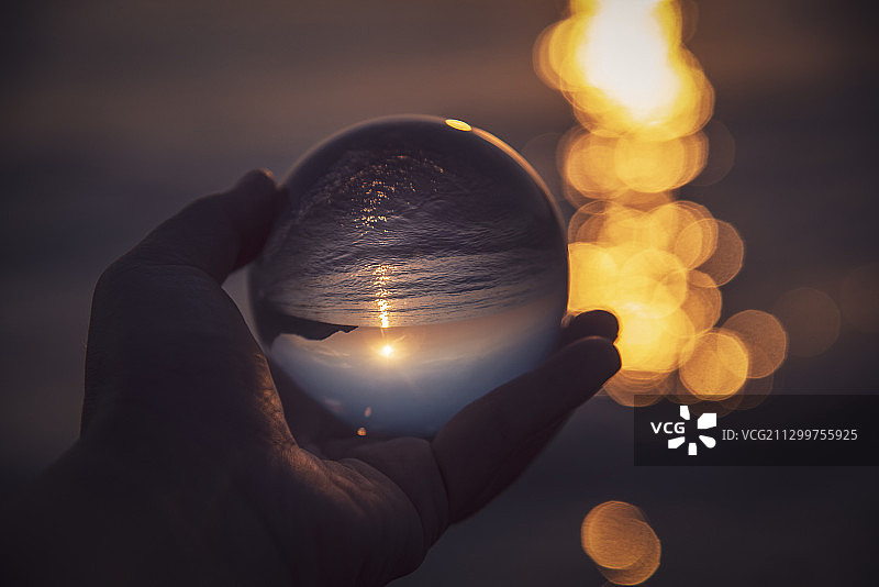 手持水晶球，日落时分的海面，意大利马泰拉，巴西利卡塔图片素材