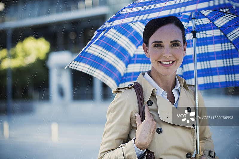 微笑的女商人穿着风衣，撑着雨伞图片素材