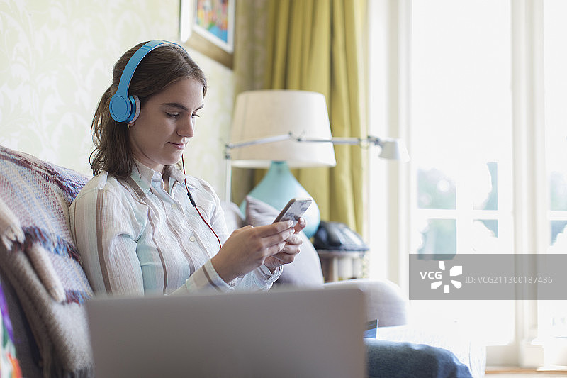 少女戴耳机在沙发玩智能手机图片素材