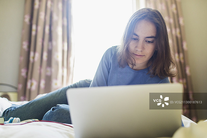 少女在阳光明媚的卧室的床上使用笔记本电脑图片素材