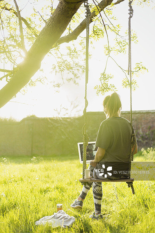 在阳光明媚的花园秋千上用笔记本电脑进行视频聊天的女人图片素材