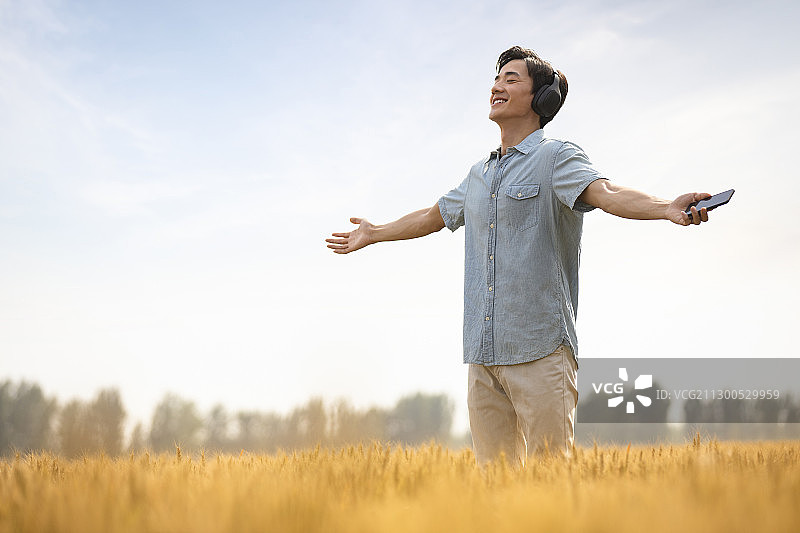 快乐的年轻男士在麦田里戴着耳机听音乐图片素材