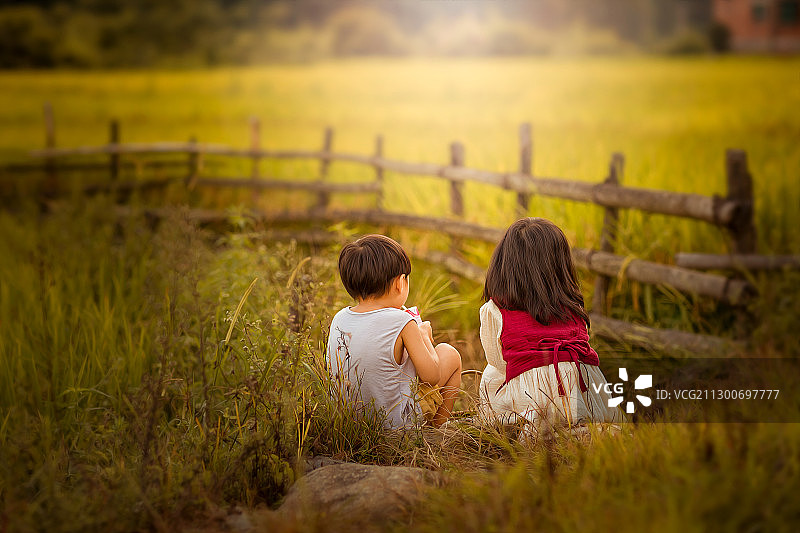 夕阳下姐弟俩坐在田埂上看着金黄色的田野图片素材