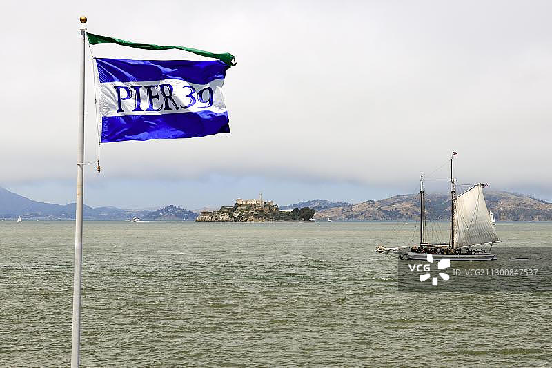 美国旧金山渔人码头39号码头的旗帜和历史悠久的帆船，背景是恶魔岛图片素材