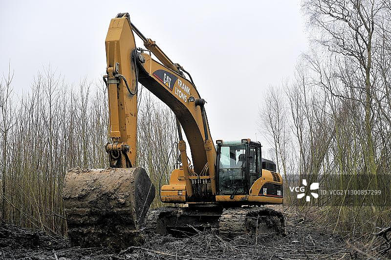 一辆大型挖掘机试图将另一辆较小的挖掘机从泥地里拉出来图片素材