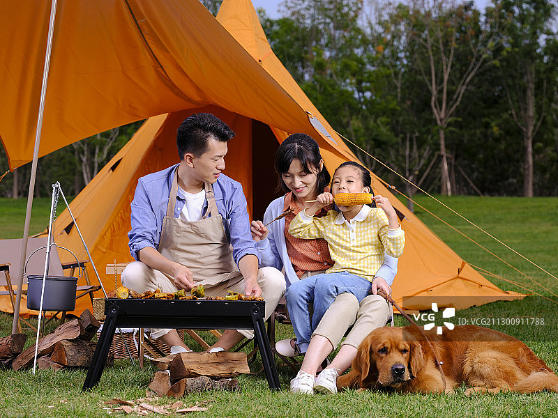 快乐的三口之家和宠物狗在公园烧烤图片素材