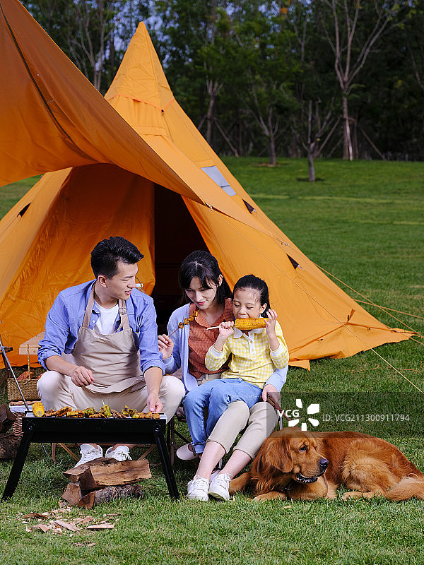 快乐的三口之家和宠物狗在公园烧烤图片素材