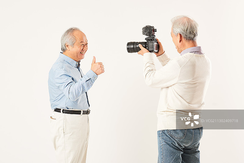 老年男人拿着相机拍摄另一位做手势的老年男人图片素材