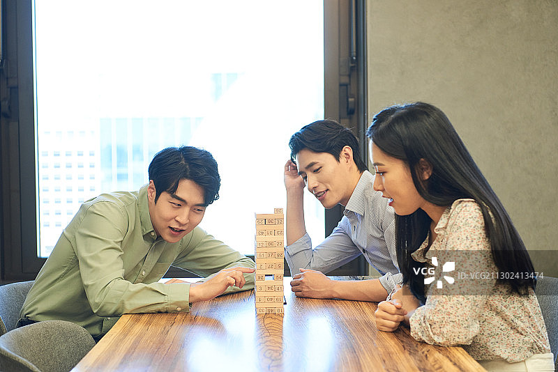 在办公室休息室里，三位同事坐在桌旁玩层层叠图片素材