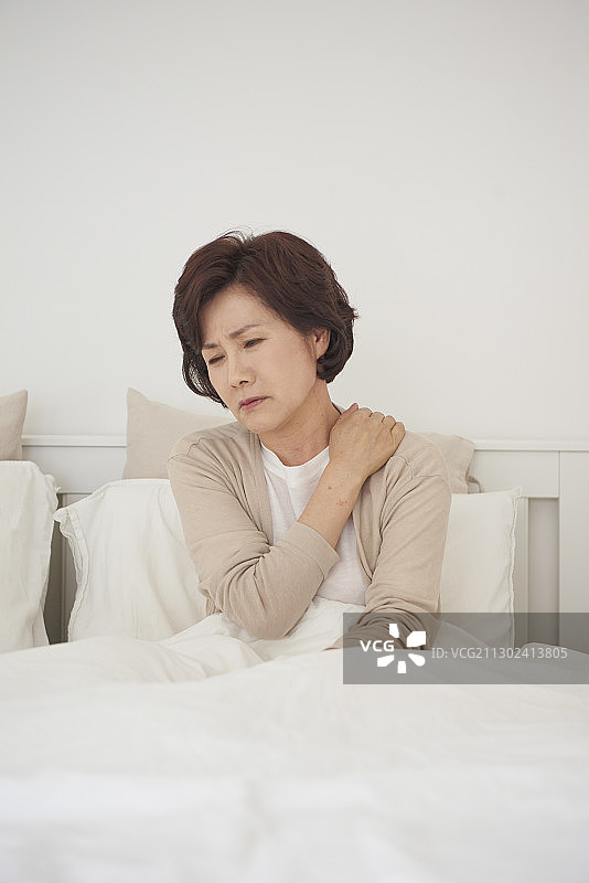 中年妇女坐在床上，肩膀疼痛，表情沮丧图片素材