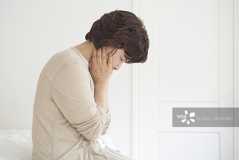 中年妇女坐在床上感到疼痛，看起来很沮丧图片素材