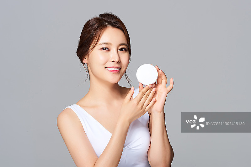 年轻女子在灰色背景上手持气垫微笑图片素材