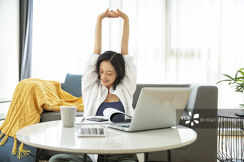 年轻女子在客厅伸懒腰居家远程办公图片素材