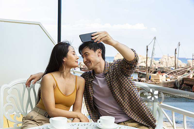 甜蜜情侣在海边度假酒店阳台喝咖啡拿手机自拍嬉戏图片素材