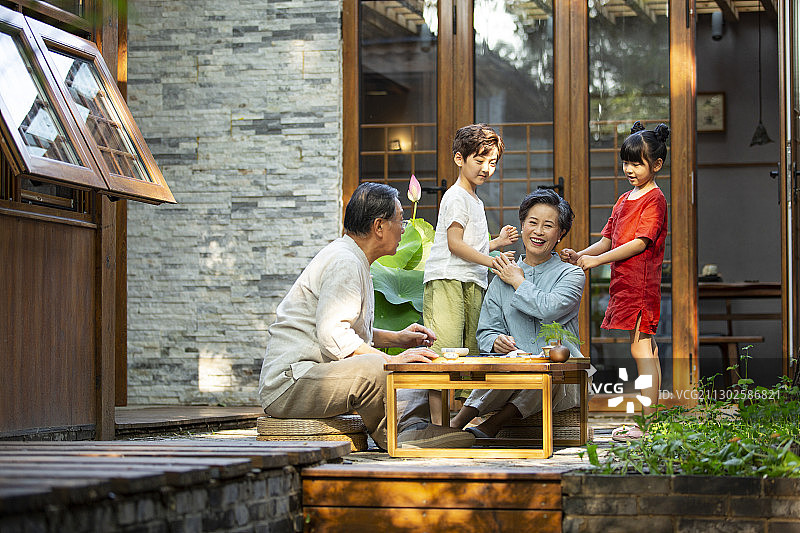 孙子、孙女给爷爷、奶奶捶背按摩在户外庭院图片素材