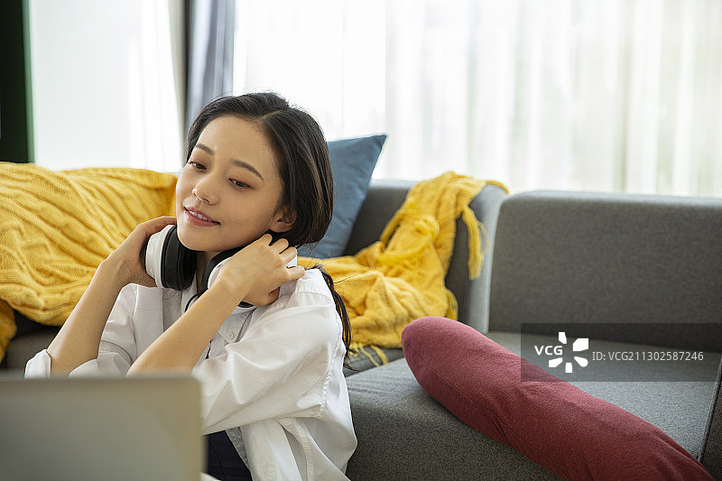 青年女子在客厅远程办公戴耳机休息放松图片素材