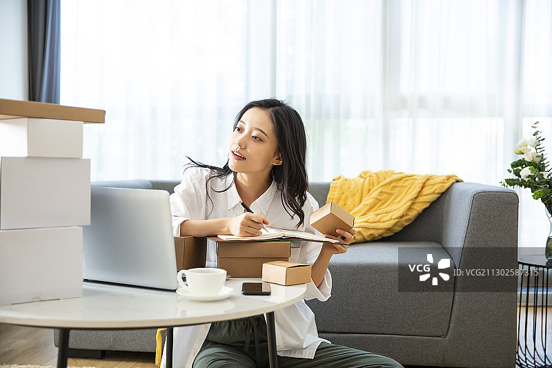 年轻女子在客厅拿着快递盒子记录信息图片素材